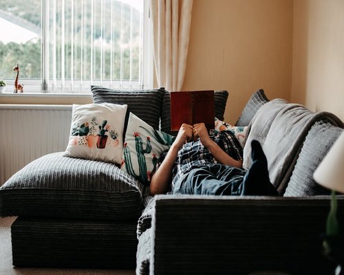 Person resting on a comfortable sofa reading a book with soft natural light